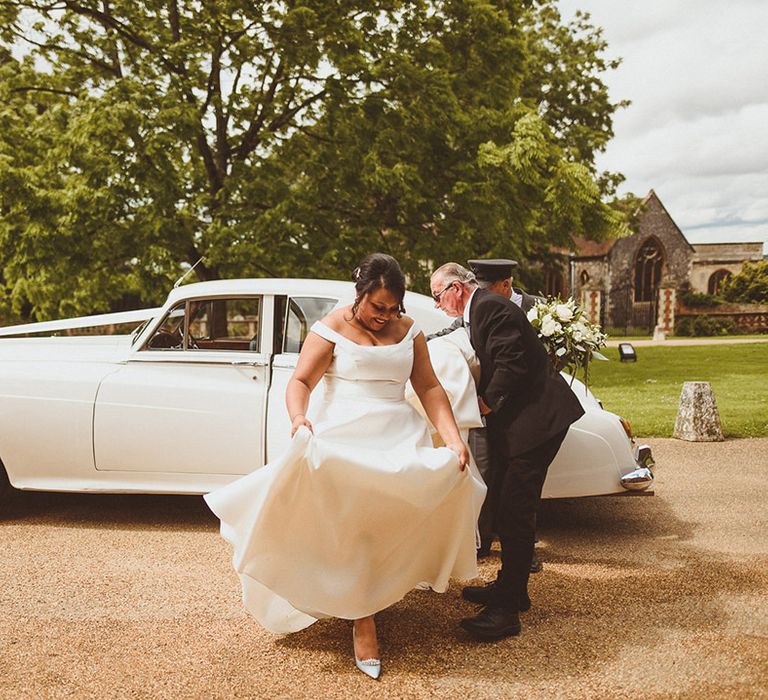 Bride exits her white wedding car transportation in her white bardot wedding dress and Jimmy Choo wedding shoes 