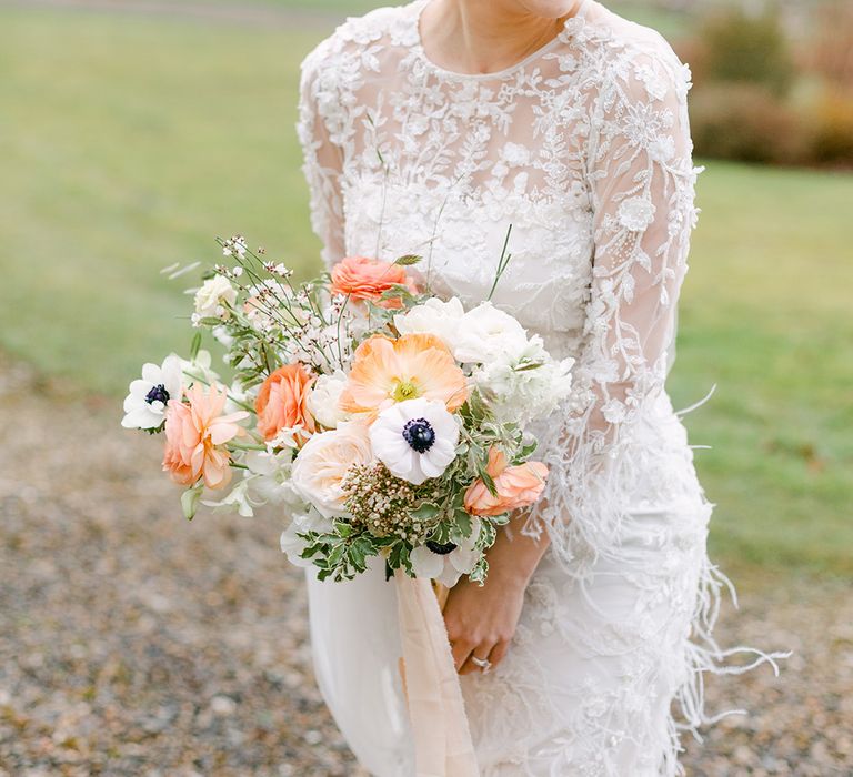 Bride in a an applique and feather wedding dress holding a peach and white flower bouquet with Icelandic poppies and anemones 