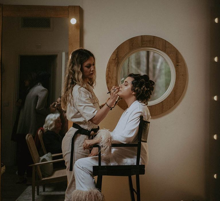 Bride in light pink feather pyjamas gets her makeup done for her wedding day 