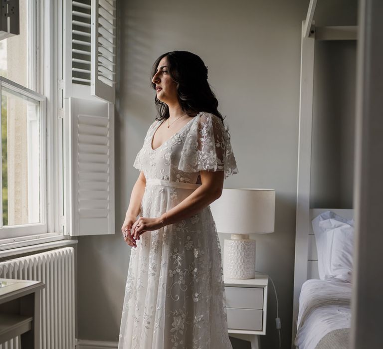 Bride looks out window wearing Anna Campbell floral embellished wedding dress with boho vibe 