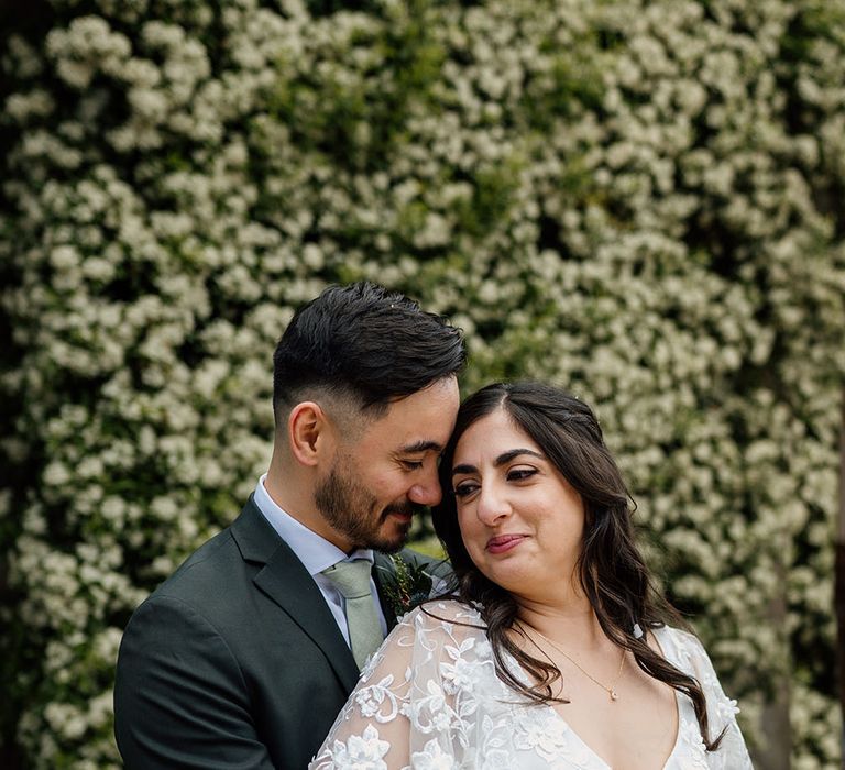 Groom wearing green tie wraps his arms around bride wearing boho wedding dress with V shaped neckline and silk tie to waist