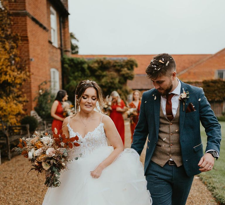 Bride carrying autumnal bouquet in a Blush by Hayley Paige wedding dress with groom in blue suit and burnt orange tie 