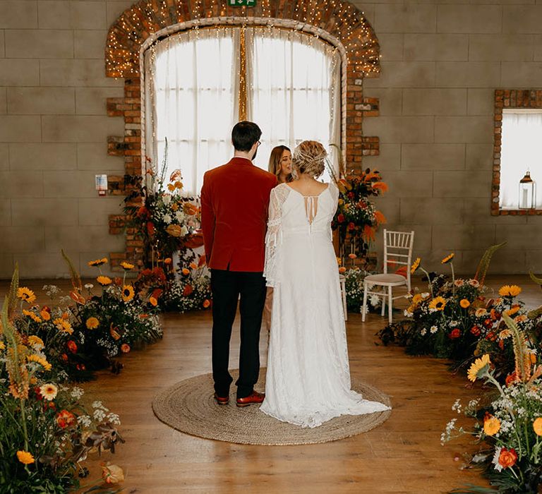 Orange and yellow wedding flowers decorate the wedding venue with bride and groom standing for the ceremony 