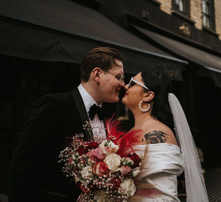 Bride wears pearl hoop earrings and floor-length veil and holds bright floral bouquet 