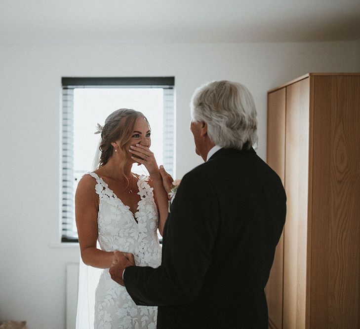 Bride wearing lace Enzoani wedding dress becomes emotional with her father on the morning of her wedding day