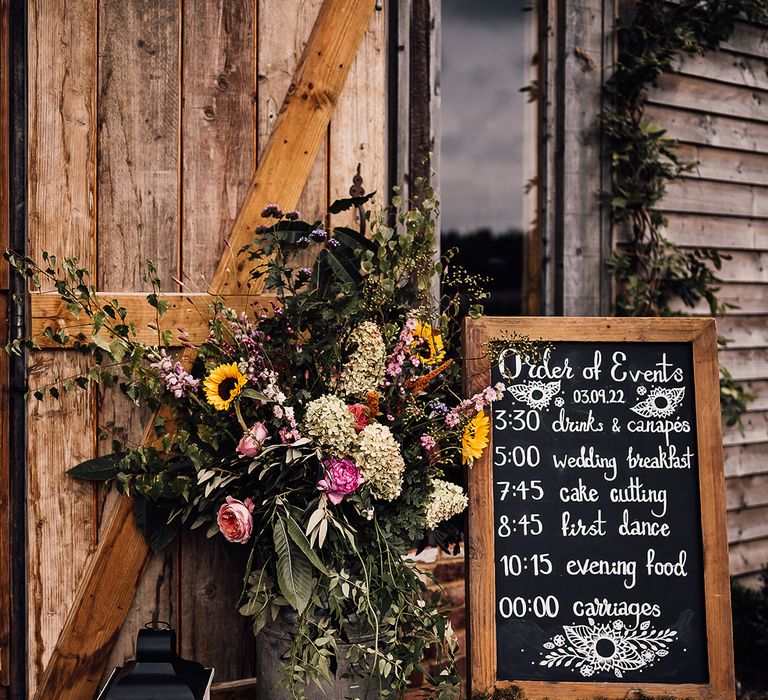 Black and white chalk board wedding order of the day sign with pink and yellow wedding flowers with candles in lanterns