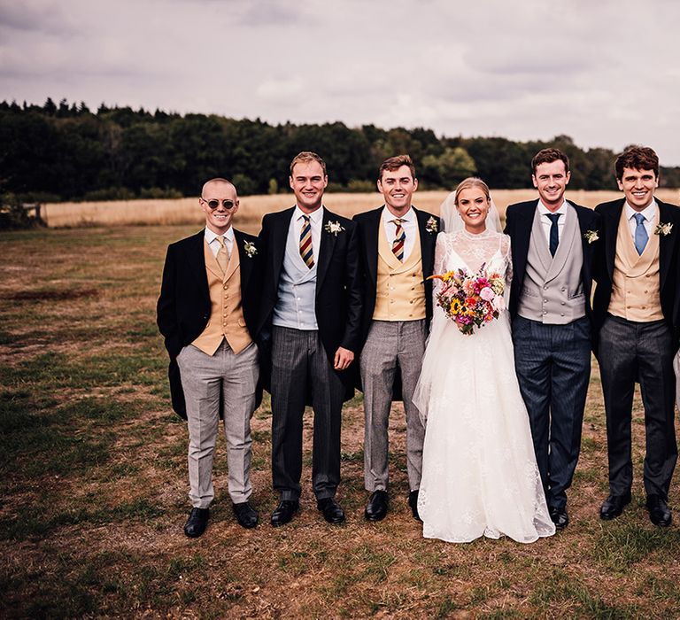 Bride with the groom and groomsmen who wear morning suits with different coloured waistcoats and ties