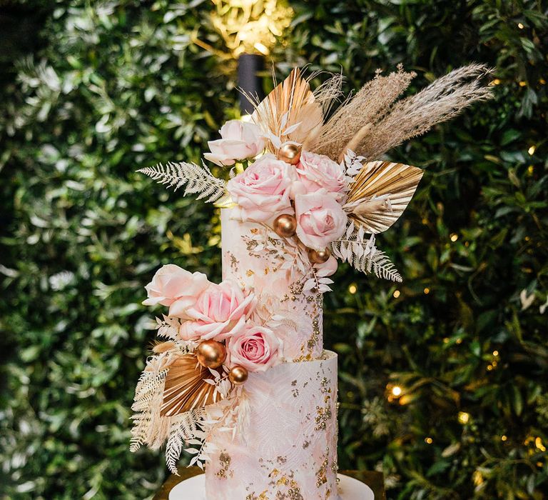 Sparkly pink and white wedding cake with gold flakes on a box of fairy lights 