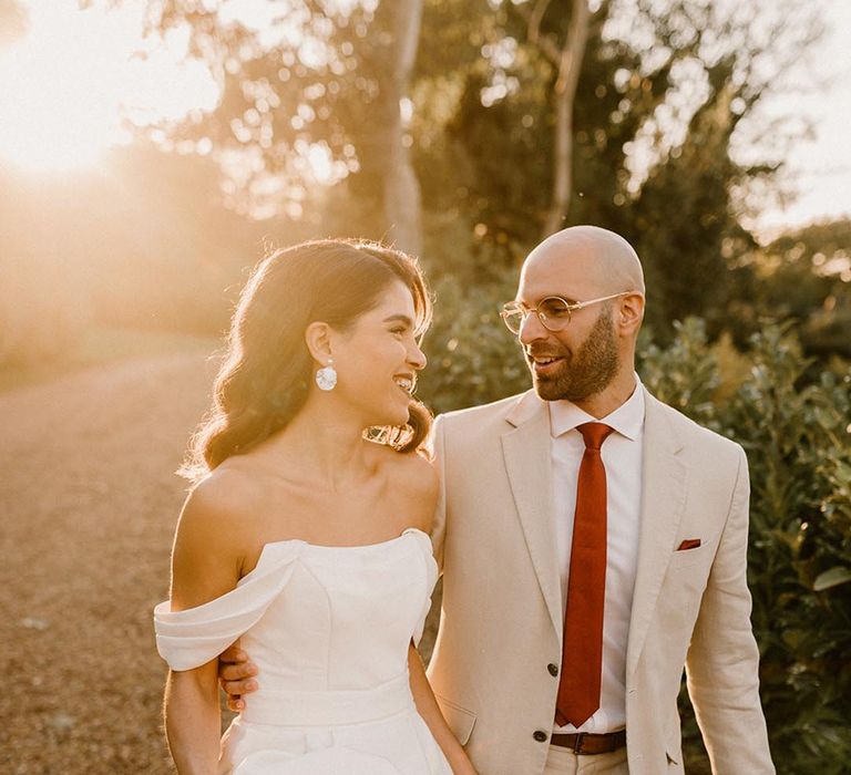 Bride in a structured off the shoulder wedding gown with the groom in a pale wedding suit and red tie for autumnal wedding at Chapel House Estate