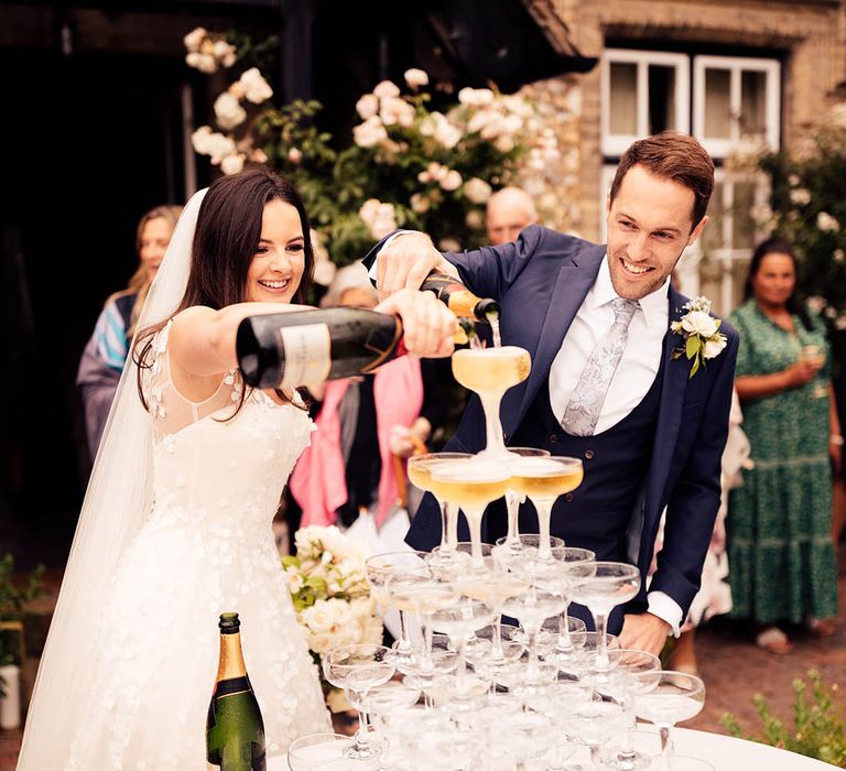 Bride and groom pour champagne over their champagne tower decor 