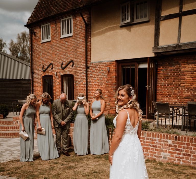 Each bridesmaid wears a sage pleated bridesmaid dress standing with the father of the bride as they hide their eyes before the first look 