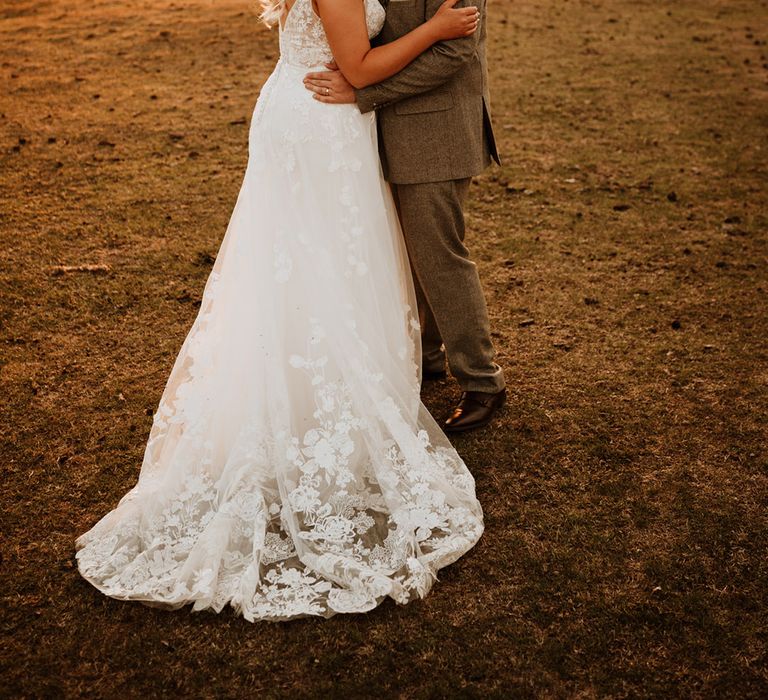 The groom in a grey tweed suit kisses the bride in a flower lace wedding dress on the cheek 