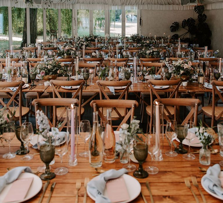 Marquee wedding reception with disco balls with decorative greenery and a pastel theme wedding table setting with blue napkins and pink menus 