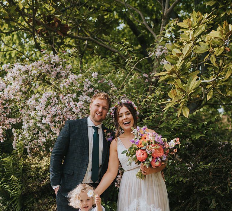 Bride wears scallop lace wedding dress and stands with her groom and son outdoors during DIY wedding