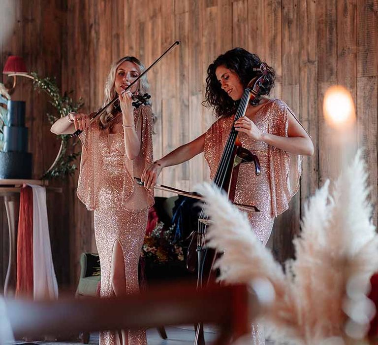 String trio playing the violin and the cello by three-tier wedding cake in a rich blue buttercream with a velvet effect base tier and gold rice paper sails, finished with a semi-circle Bramble Sky arch stand