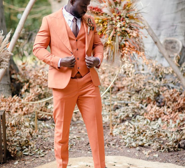 Groom in burnt orange rust coloured suit with brown tie, pocket square, brown accessories and dried flower, rose and pampas grass boutonniere  