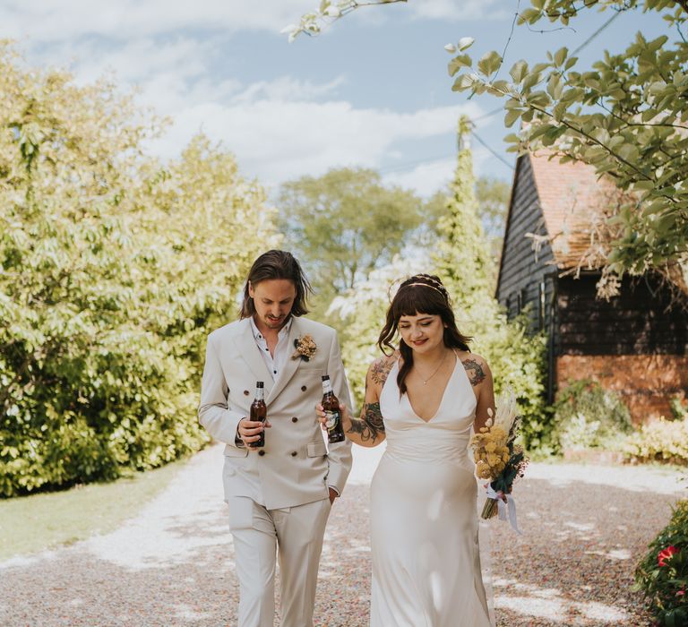 Bride and groom in ASOS outfits with dried floral bouquet having some beer 