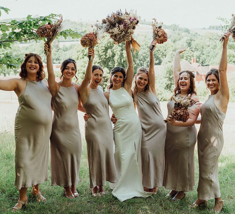 Bridesmaids in halter neck champagne gold dresses with the bride also in a white halter neck wedding dress holding boho bouquets with bunny grass