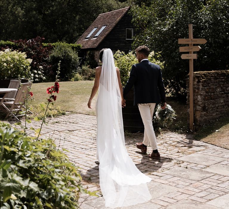 Bride in floor-length veil walks alongside her groom at the Gate Street Barn rustic wedding venue 