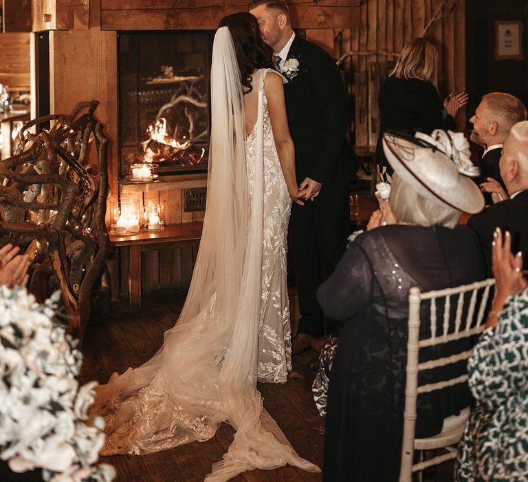 The bride and groom share their first kiss as a married couple s the wedding guests clap for their rustic treehouse wedding 