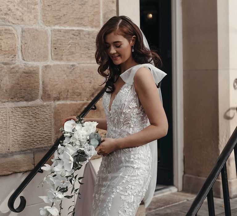 Bride holding a white orchid and rose cascading wedding bouquet wearing a sparkly floral wedding dress 