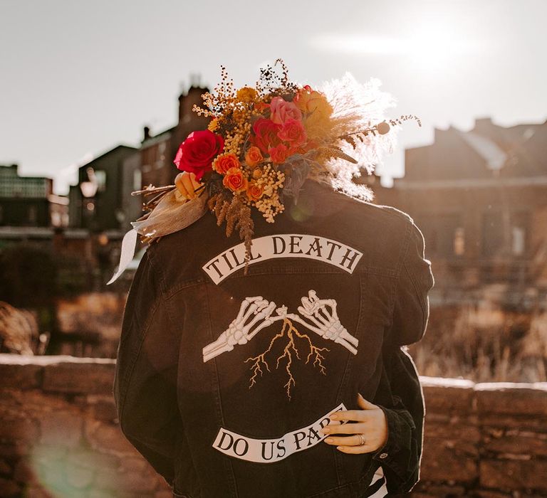 Groom wearing personalised black denim jacket with skeleton hands and "Til Death Do Us Part" lettering 