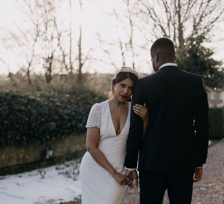 Bride in v neck short lace sleeve wedding dress with front slit and button detailing holding hands with groom in black suit standing in the grounds of Manor House wedding venue in Yorkshire 