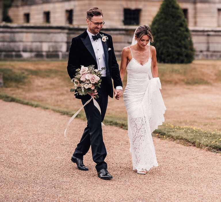 The groom in a black velvet tuxedo carries the bride's pink garden rose bouquet with the bride in a Grace Loves Lace dress for the Hanley Hall Worcestershire wedding 