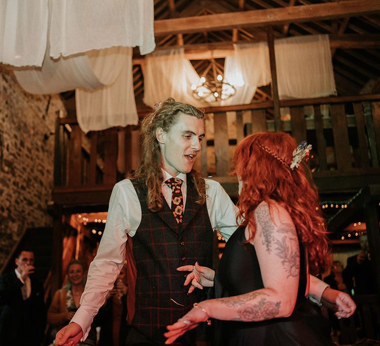 Groom in checkered dark grey waistcoat, white shirt and burgundy flower patterned tie dancing with bride in black wedding dress to live wedding band 