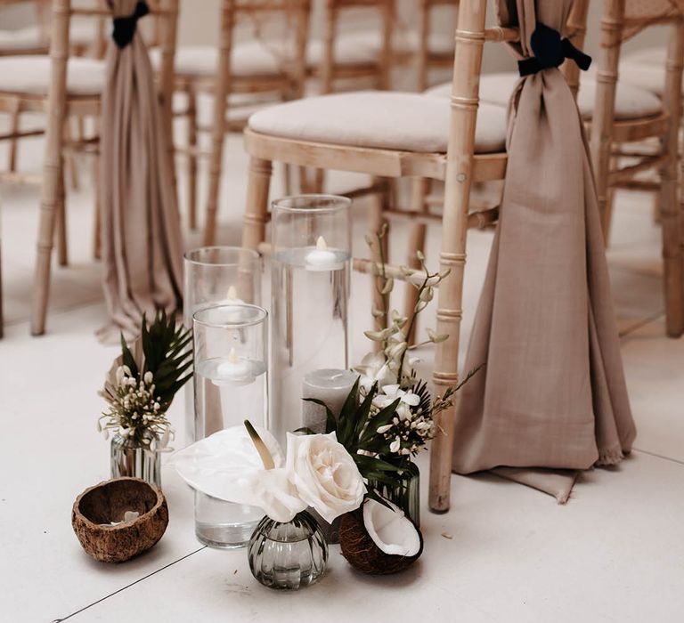 White anthuriums, roses, palm leaves in glass jars with coconuts and floating tea lights in hurricane vases 