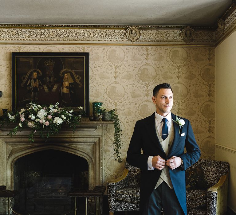 Groom in black morning suit with beige waistcoat and navy tie with silver tie clip for the wedding day 