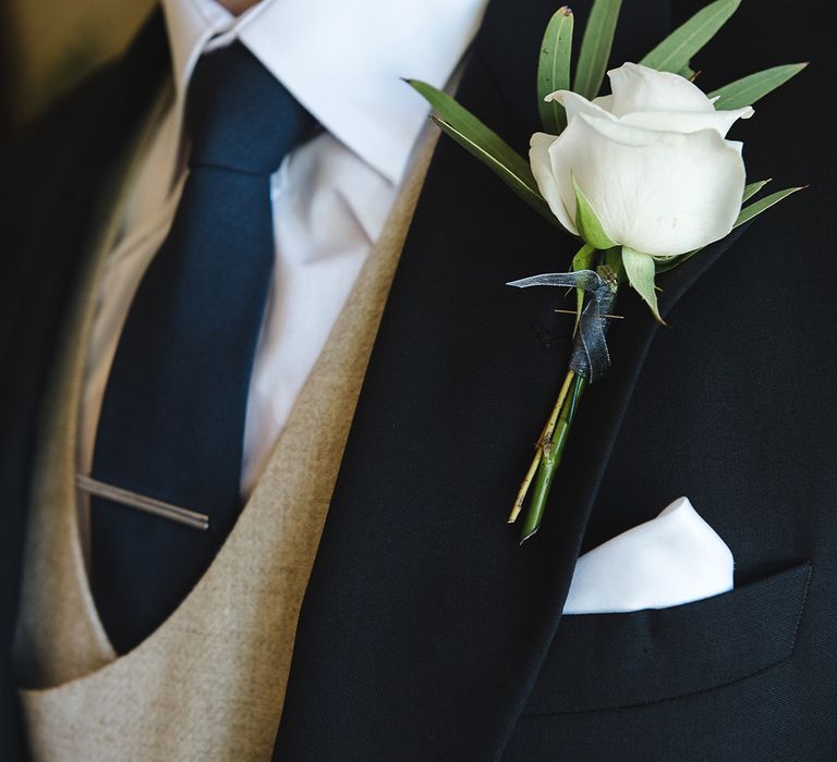 Simple white rose buttonhole worn by the groom in a morning suit for the traditional wedding 