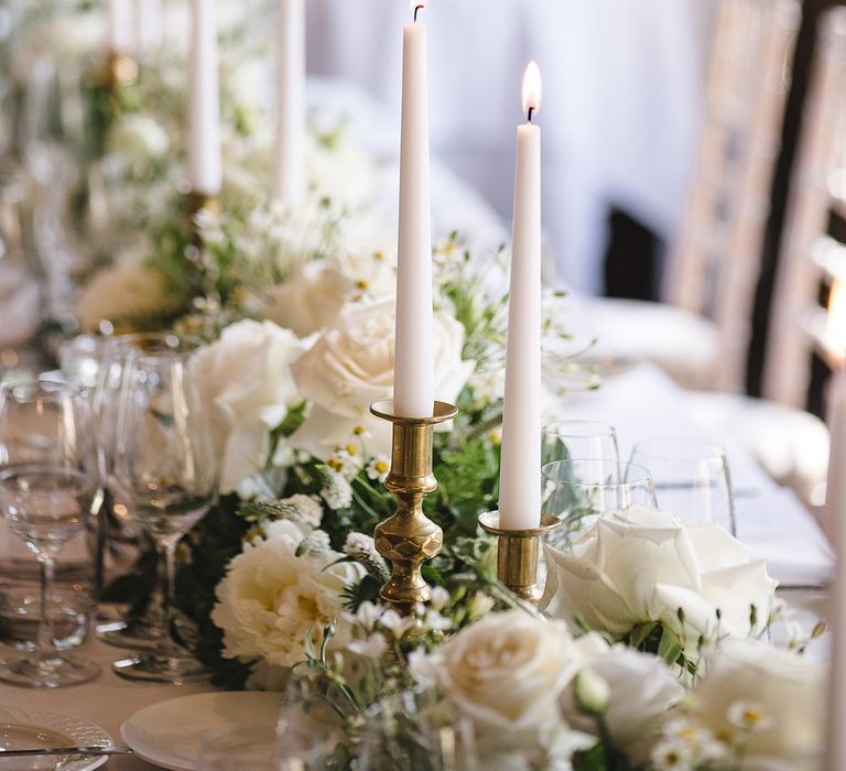 White taper candles in gold candle holders on the wedding table with white wedding flower table decorations 