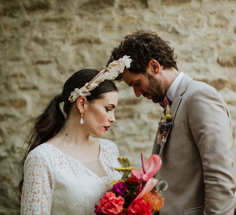 Bride in white floral bridal crown and red lip bridal makeup, holding pink bridal bouquet with groom in greige suit at outdoor wedding in Italy