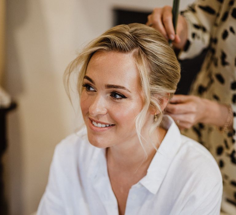 Bride wearing white pyjamas sits down as she gets her hair and makeup done for the wedding day 