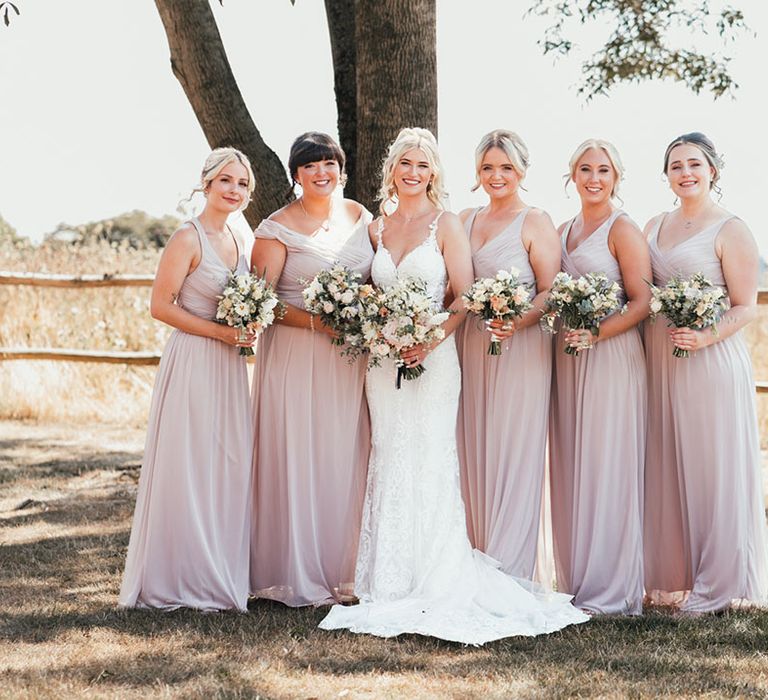 Pink bridesmaid dresses posing with the bride in a fitted lace wedding dress holding white wedding bouquets 