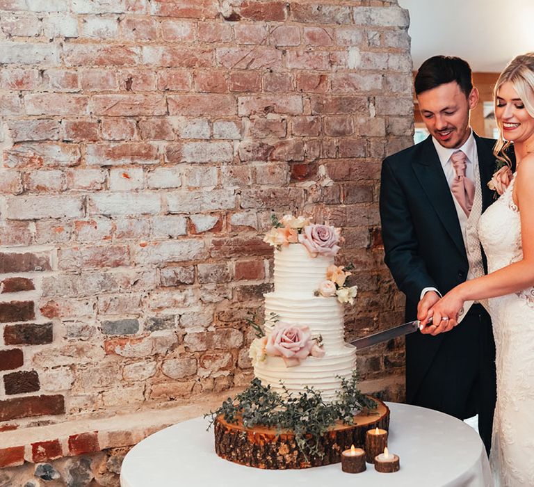 The bride and groom cut their three tier white iced wedding cake together with rose cake decorations 