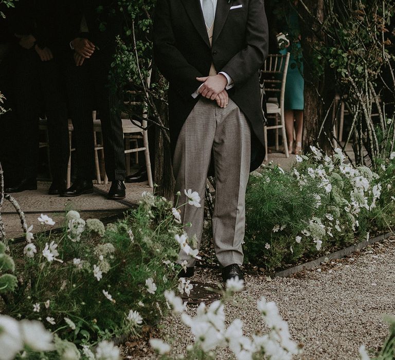 Groom in black morning suit with grey trousers smiles as he sees the bride for the first time in her outfit 