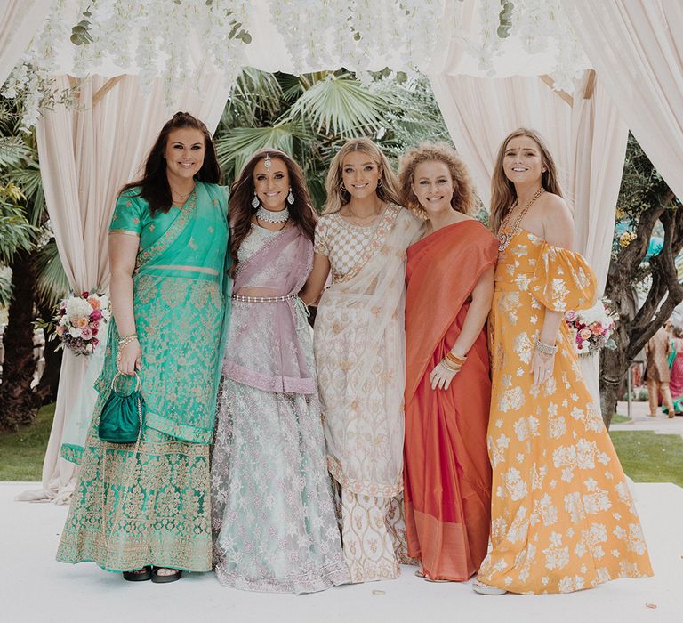 Bridal party standing in the wedding mandap wearing mismatched bridesmaid lehengas and bride wearing mint green and dusky pink ombre embellished lehenga 