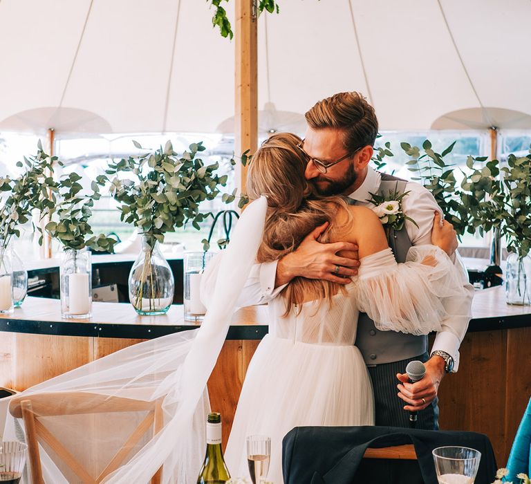 The bride hugs the groom in his grey waistcoat after delivering the groom speech 