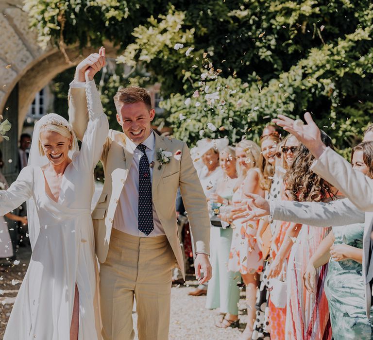 Confetti moment with bride in a long sleeve Emma Beaumont wedding dress and groom in a beige suit 