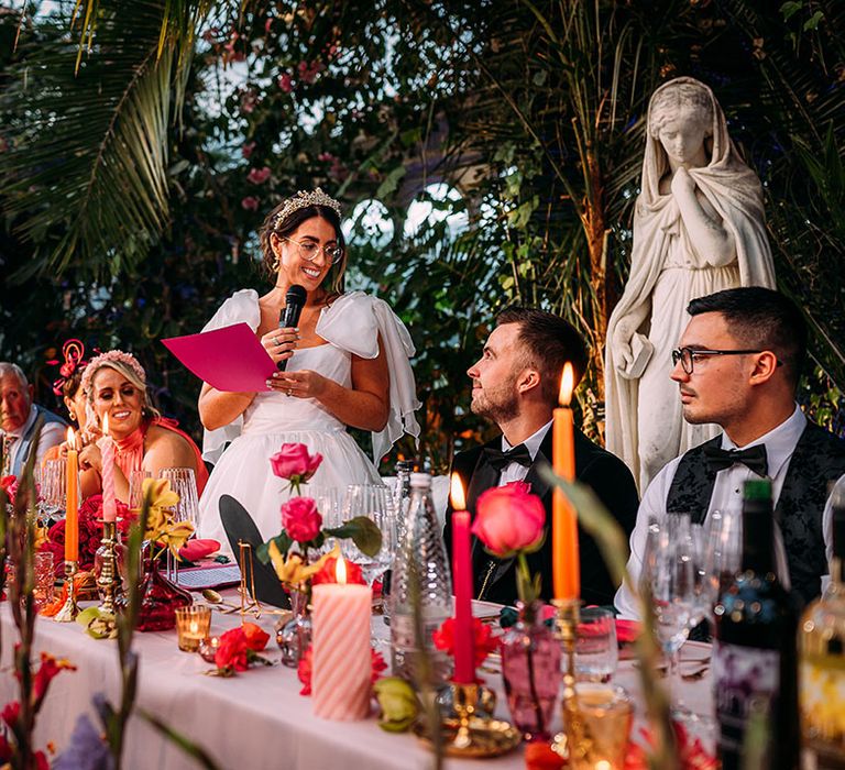 The bride in a ruffle wedding dress stands reading out her bridal speech at the wedding 