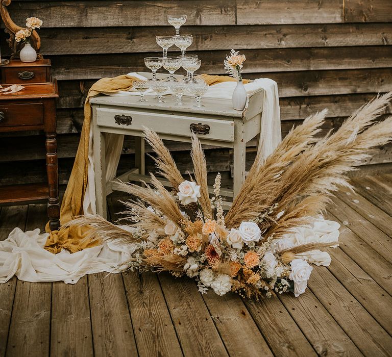 champagne tower on a vintage dresser with pampas grass a muted flower arrangement 