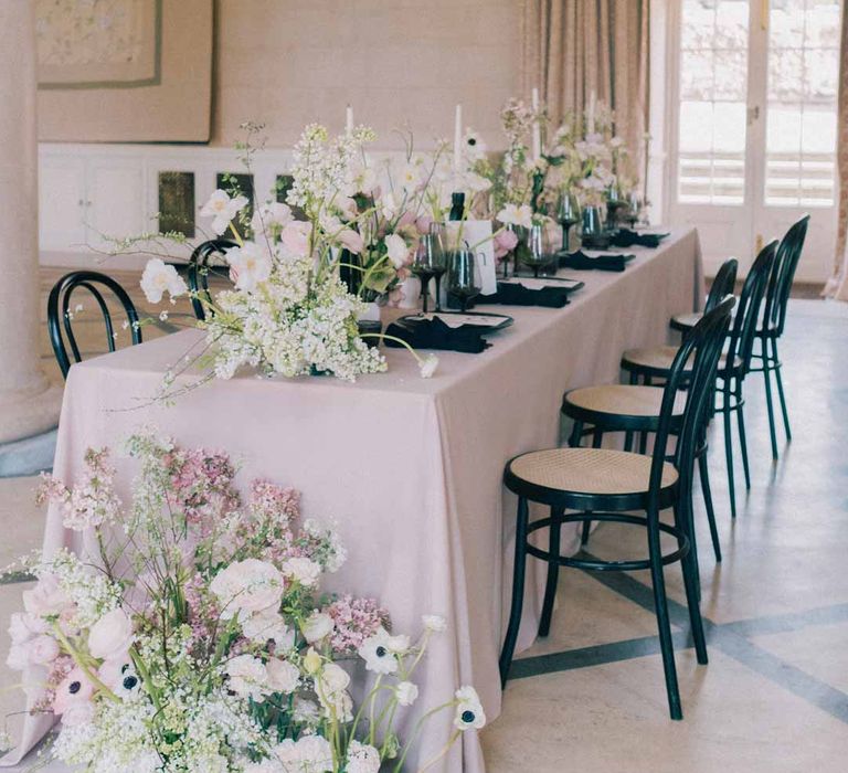 Notan inspired wedding tablescape consisting of light pink wedding tablecloth, white poppies, light pink Persian buttercups, baby's-breath and foliage centrepieces, black artistic candlestick holders, white tapered candles, black crockery and monochrome wedding stationery at Settrington Orangery