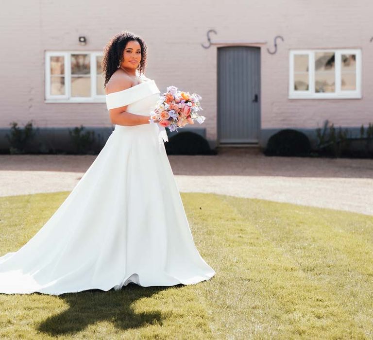 Bride in off the shoulder wedding dress with puddle train holding orange, lilac and peach mixed flower bridal bouquet on the grounds of Rackleys Barn wedding venue