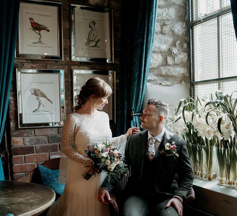 The 6 month pregnant bride looks down at the seated groom as they pose for couple portraits on their wedding day 