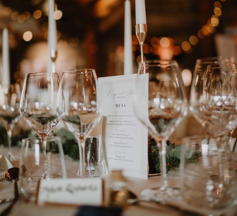 Classic wedding tablescape with forest green napkins, white wedding tablecloth, white tapered candles and minimalistic wedding stationery and menus at La Cabane Des Praz wedding venue