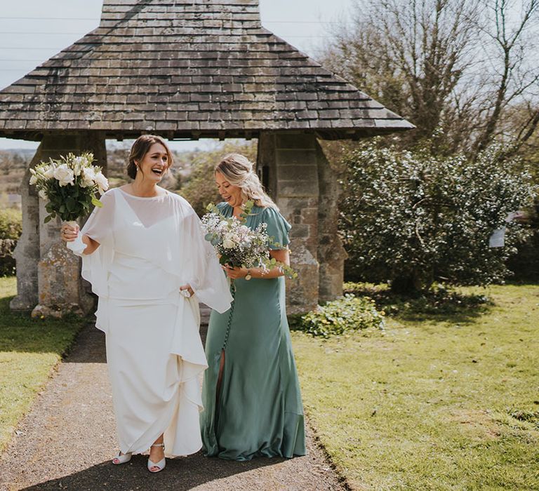 Maid of honour in satin green short sleeve bridesmaid dress walking with the bride to the church 