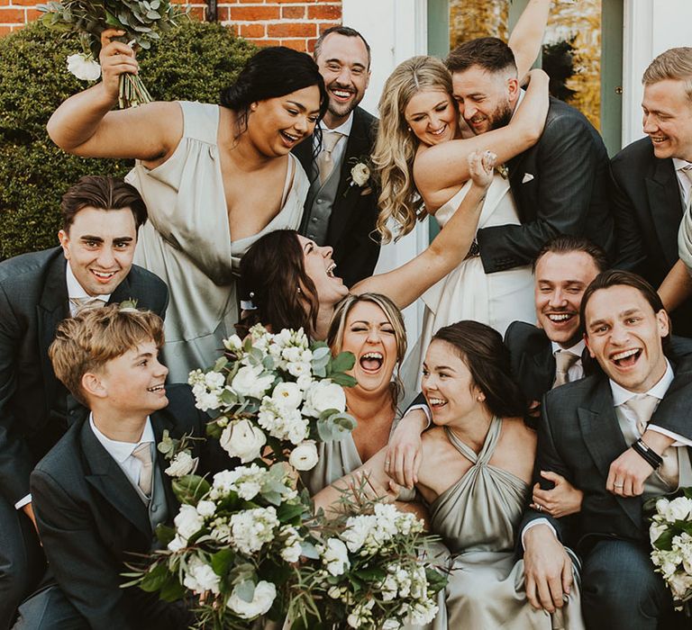 The wedding party all squeeze into a photo together in green bridesmaid and groomsmen wedding outfits 