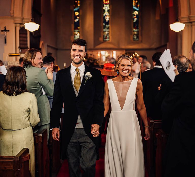 Groom in traditional wedding morning suit with yellow tie walking hand in hand with bride in Andrea Hawke wedding dress 